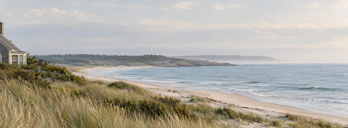 A quiet coastal cottage, sandy shoreline and soft blue sea.